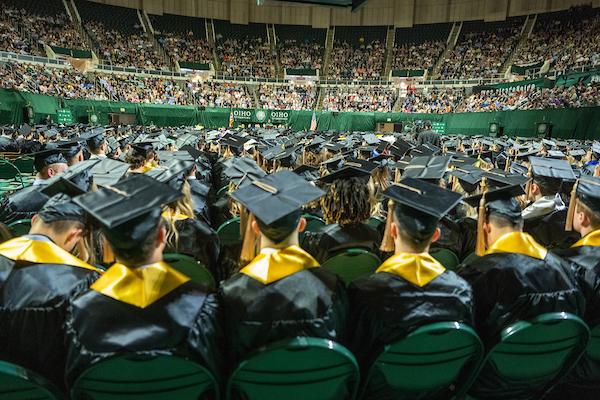 Students wearing caps and gowns sit together during Commencement